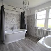 BATHROOM: Wood grain effect tiling and roll top bath with wall mounted mixer tap.