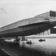 The HMA1 (Mayfly) emerges from its shed on Cavendish Dock in 1911 with sailors in rowing boats underneath.