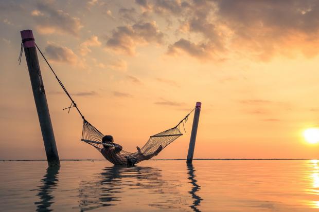 The Mail: A man relaxing over the water in a hammock. Credit: Canva